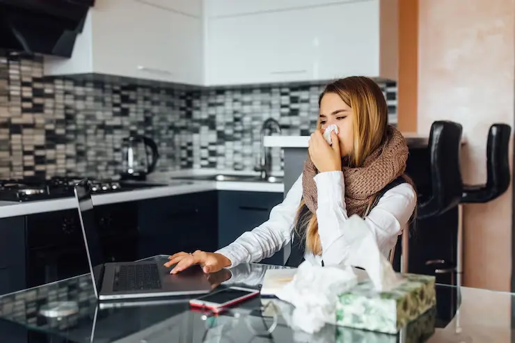 sick-business-woman-sitting-table-home-blows-his-nose-while-using-laptop_